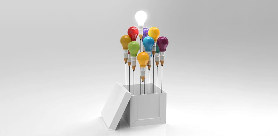 An open white box with colored light bulbs attached to springs emerging from it. Each bulb is a different color, including red, orange, yellow, green, blue, purple, and one white bulb that is lit, glowing brightly above the others against a plain gray background.