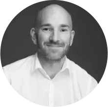 Smiling bald man with a beard wearing a white shirt, facing the camera.