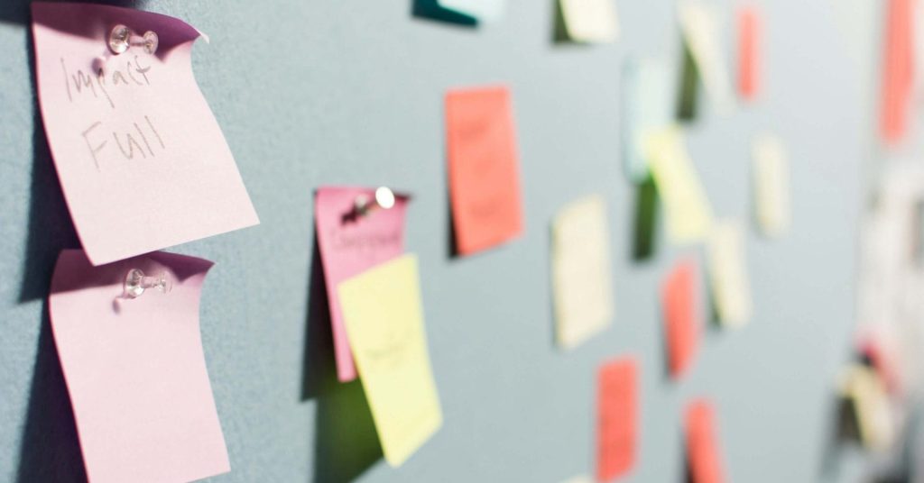 Colorful sticky notes are pinned to a gray wall, some with handwritten text visible.