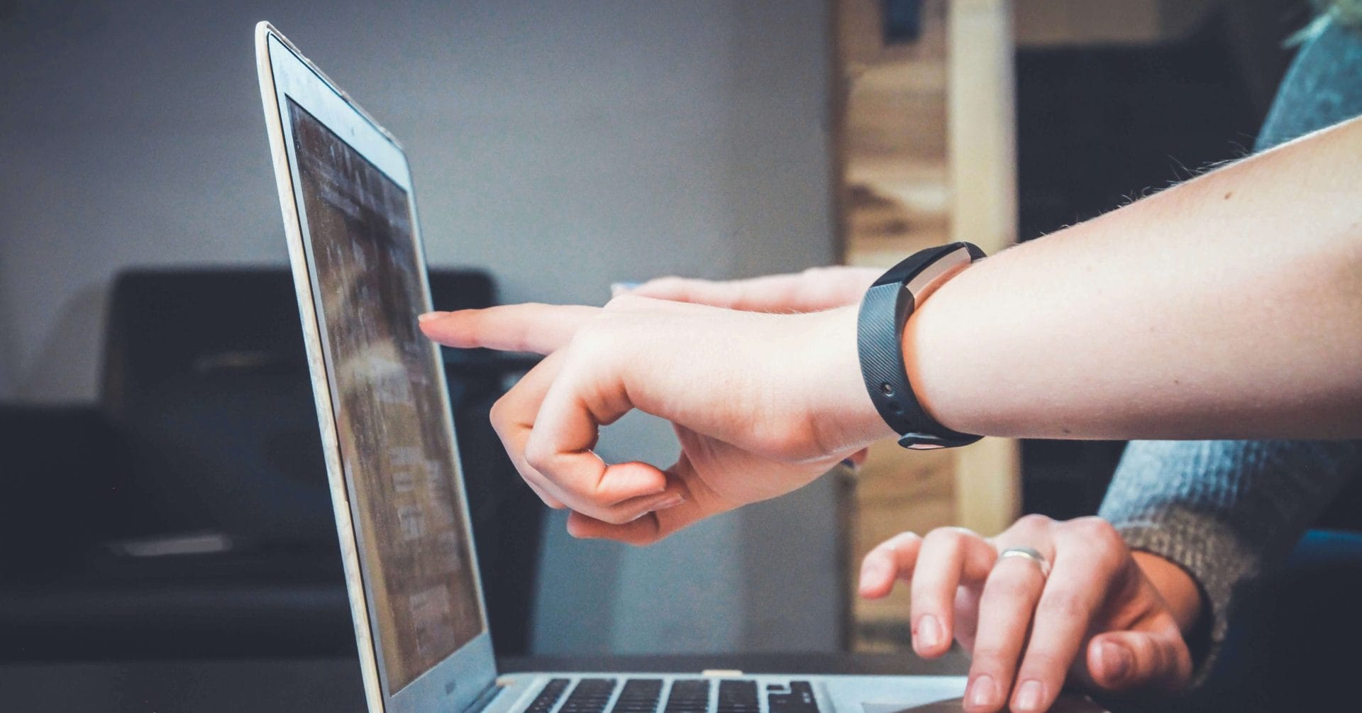 Two people use a laptop; one points at the screen while the other types on the keyboard.